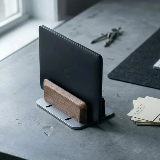 Adjustable walnut vertical laptop stand with a metal base holding a laptop on a desk.
