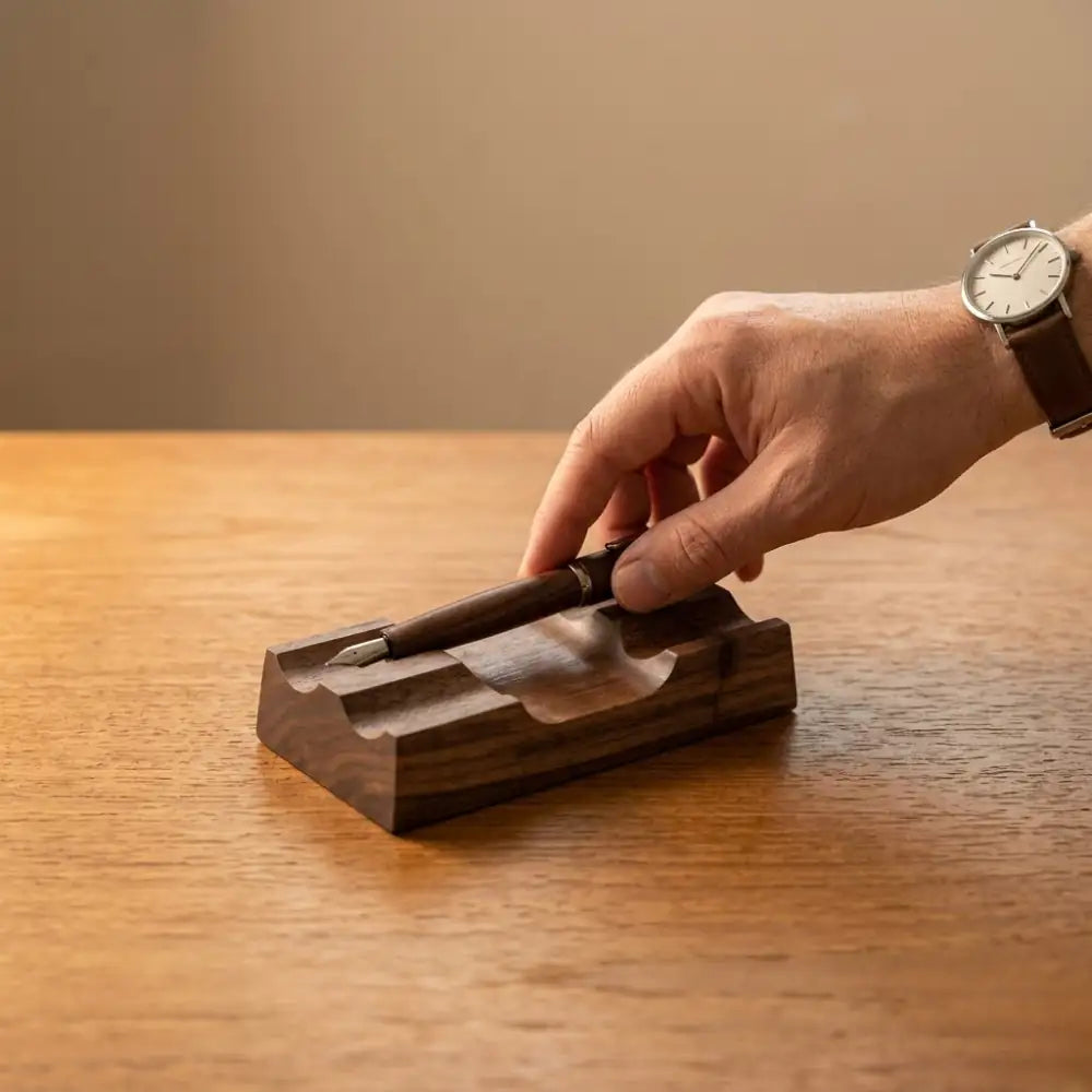 Hand placing a fountain pen onto a solid walnut desk pen rest