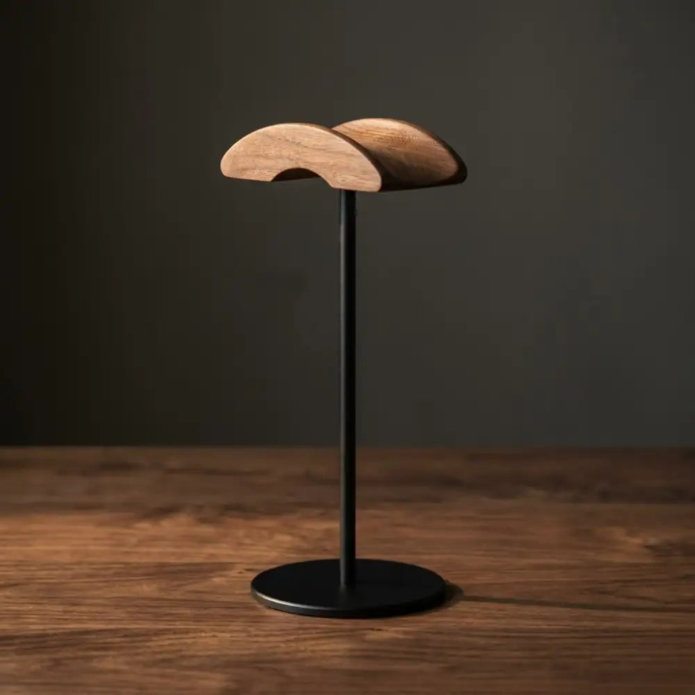 Walnut headphone stand with curved top on a dark background