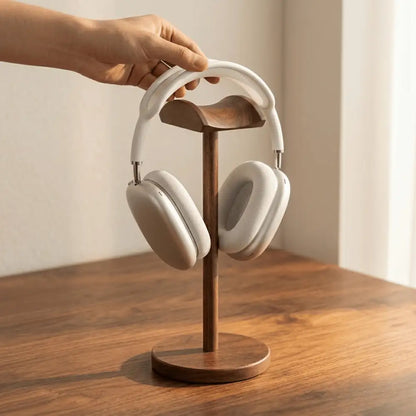 Hand placing headphones onto a walnut headphone stand on a desk