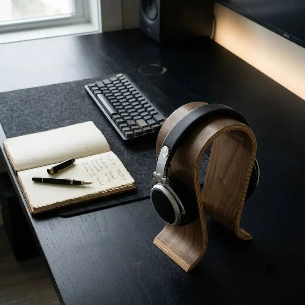 U-shaped wooden headphone stand holding black headphones on a home office desk.