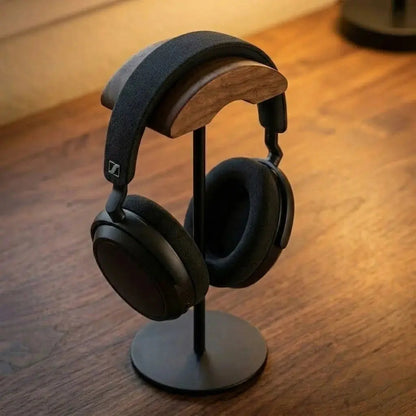 Walnut headphone stand with black finish holding over-ear headphones on a wood desk