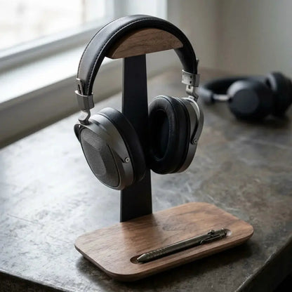 Walnut headphone stand with pen tray holding over-ear headphones and a pen on a desk