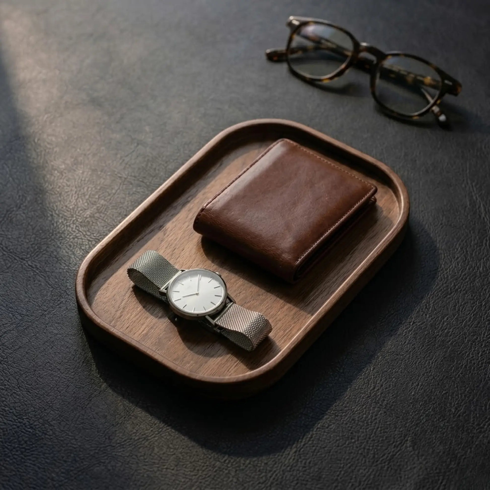 Solid walnut valet tray for desk setup holding a leather wallet and wristwatch on a dark desk surface