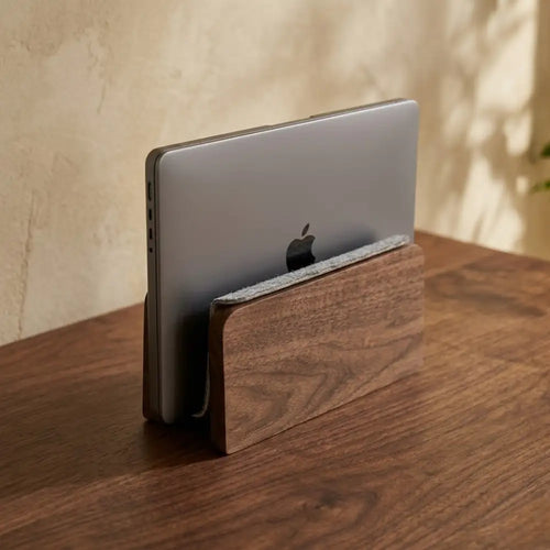 Minimalist walnut vertical laptop stand securely docking a MacBook on a warm wooden desk